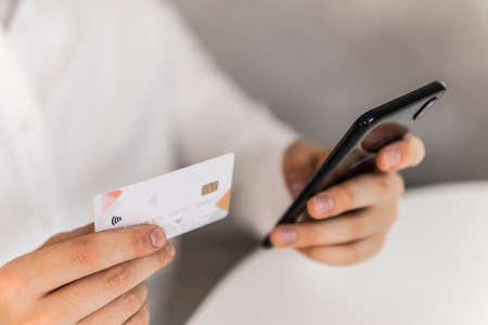 Online shopping concept in morning light. Closeup of young man making man hands using smartphone and holding credit card with social Payment online shopping smartphone at working place.の写真素材