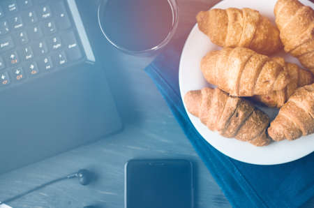 Closeup of wooden desktop with coffee, croissant, phone with headphones and notepadの写真素材