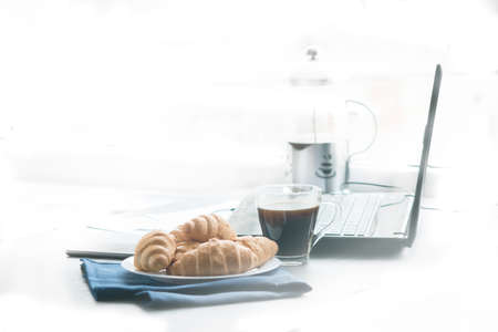 Closeup of wooden desktop with coffee, croissant, phone with headphones and notepadの写真素材