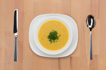 A plate of traditional Indian and Pakistani first course - Mili Juli soup - decorated with potherbs on a wooden table with spoon and knife.の写真素材