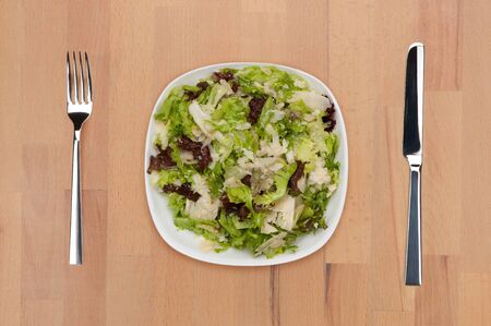 A plate of green lettuce salad with fork and knife on a wooden table.の写真素材