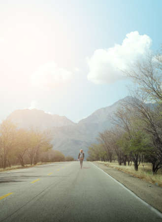 Traveler in the middle of the road with a backpack and mountains in the background on a sunny day.の写真素材