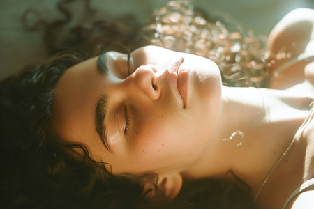 A peaceful close-up of a young woman lying down, her face bathed in dappled sunlight, exuding tranquilityの素材