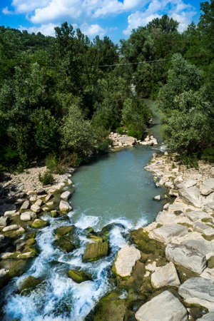 Small lake formed by the Zena torrent in Emilia, Italy, surrounded by trees, stones and rocks and creating a smooth waterfallの写真素材