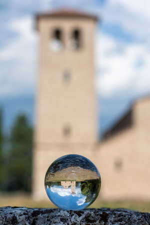 Italian summer landscape, seen through a small crystal ball, hand of man holding the lensball, ancient religious constructionsの写真素材