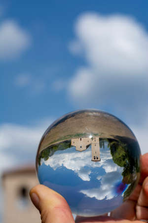 Italian summer landscape, seen through a small crystal ball, hand of man holding the lensball, ancient religious constructionsの写真素材