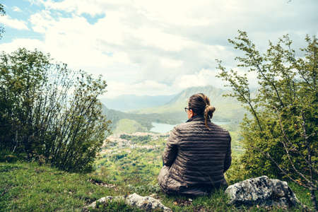Adult woman looking at the landscape in spring, view from the top of a mountain, Italyの写真素材