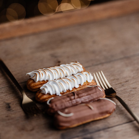 Delicious eclairs with whipped cream and chocolate on wooden background