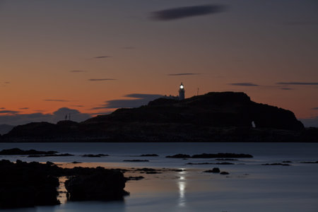 Lighthouse on Fidra island at astonishing sunset on vibrant sky background with light beam....