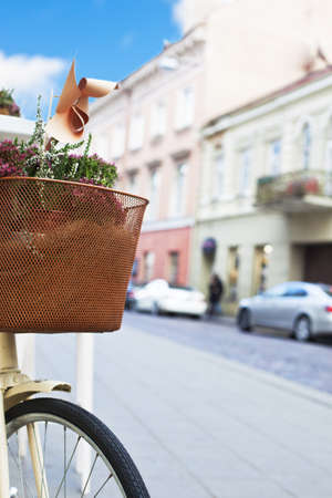 Front fragment of girlish bicycle with flowers in basket and an European old town street on the background.の写真素材