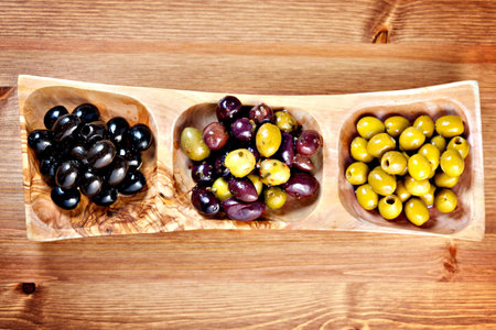 Variety of green, black and mixed marinated olives in olive tree dish on wooden table. Above point of viewの写真素材