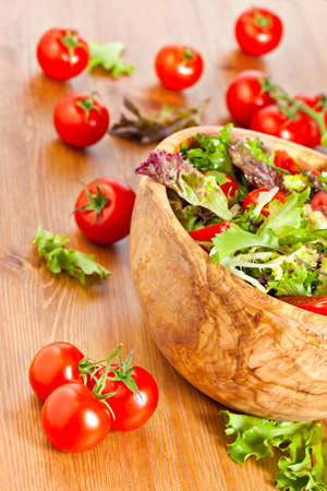 Bowl made of olive wood filled with mixed lettuce salad and cherry vine tomatoes on wooden table. More healthy food in my portfolioの写真素材