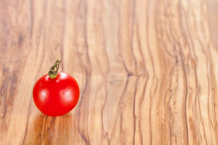 One red cherry tomato on olive oil wood surfaceの写真素材