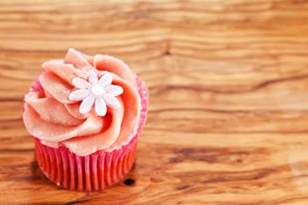 Homemade pink cupcake decorated with swirl icing and sugar daisyの写真素材