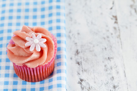 Homemade pink cupcake decorated with swirl icing and sugar daisy