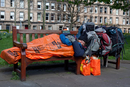 EDINBURGH, SCOTLAND - APRIL 15, 2014: Unidentified local homeless bearded man sleeps on a bench in...