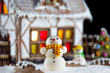 Decorative snowmen and gingerbread house with lights inside on black background. Rural Christmas night sceneの写真素材