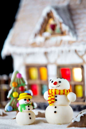 Decorative snowmen and gingerbread house with lights inside on black background. Rural Christmas night sceneの写真素材