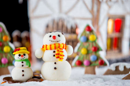 Decorative snowmen and gingerbread house with lights inside on black background. Rural Christmas night sceneの写真素材