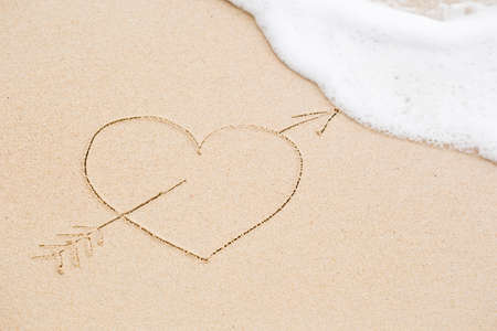Picture of a heart pierced with an arrow on wet beach sand. Concept of celebrating the St. Valentine's day at some exotic placeの写真素材