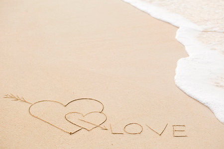 Inscription of Love with two hearts on wet beach sand. Concept of celebrating the St. Valentine's day at some exotic placeの写真素材