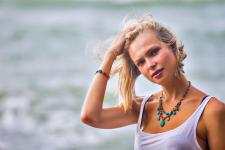 Beautiful young blonde woman posing outdoor at the rocky sea shore. Trendy fashion female model dressed in white topの写真素材