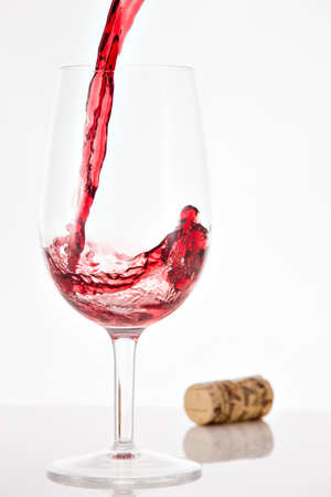 Pouring red wine into wineglass with splash on white backgroundの写真素材