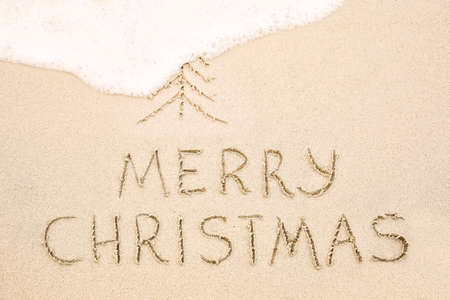 Merry Christmas inscription on wet yellow shoreline beach sand. Holiday wish messageの写真素材