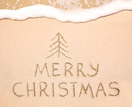 Merry Christmas inscription on wet yellow shoreline beach sand. Holiday wish messageの写真素材