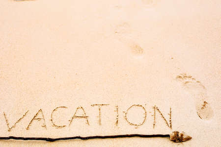 Inscription of Vacation written on wet yellow beach sand with footprint and arrow showing the directionの写真素材