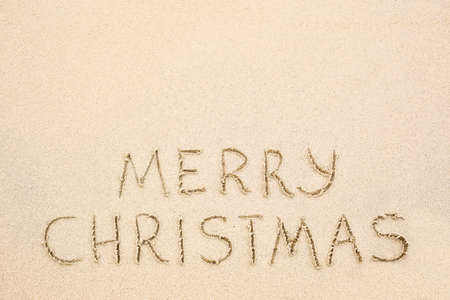 Merry Christmas inscription on wet yellow shoreline beach sand. Holiday wish messageの写真素材