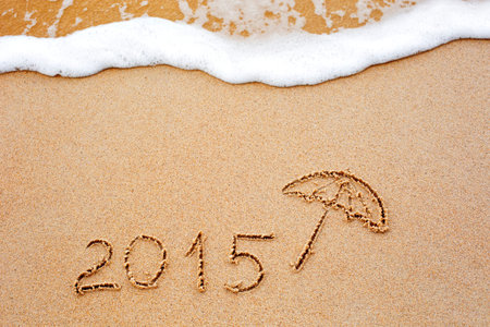 Foaming sea wave coming to wash inscription of the year 2015 written in the wet yellow beach sand. Concept of celebrating the New Year at some exotic placeの写真素材
