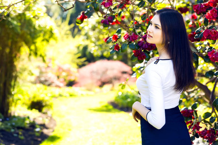 Young beautiful woman with long straight dark hair posing in spring gardenの写真素材