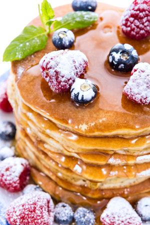 Pile of pancakes with blueberries and raspberries sprinkled with icing sugar and poured on with...