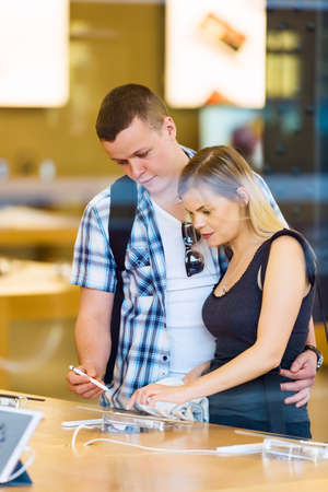 Young couple in consumer electronics retail store browsing at displayed latest tablets, choosing new device.の写真素材