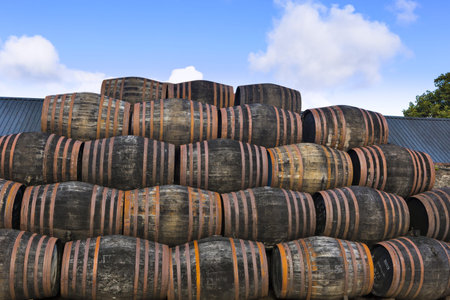 Stacked pile of old wooden barrels and casks under open sky at whisky distillery in Scotland.