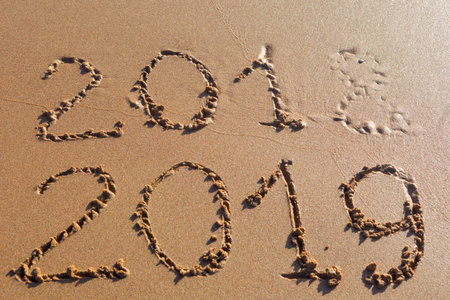 2018 2019 inscription written in the wet yellow beach sand washed with sea water wave. Concept of...