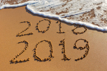 2018 2019 inscription written in the wet yellow beach sand being washed with sea water wave. Concept of celebrating the New Year at some exotic place.の写真素材