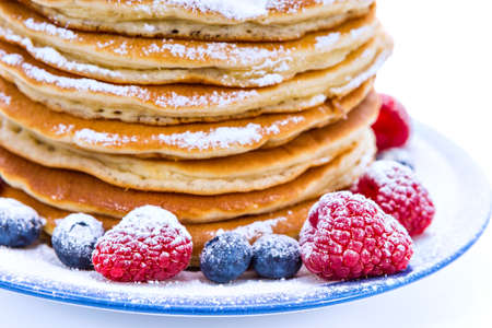 Pile of pancakes with blueberries and raspberries sprinkled with icing sugar for breakfast on white backgroundの写真素材