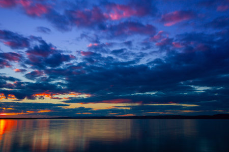 Dramatic colorful vibrant sunset sky with clouds reflected in the water.