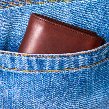 Closeup of brown leather wallet peeking out of blue jeans back pocket. Budget or luxury travel, shopping, spending concept.の写真素材