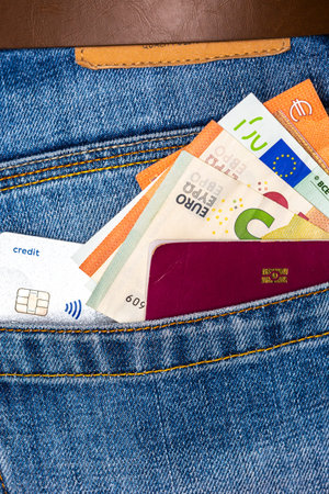 Closeup of a bunch of Euro banknotes, contactless credit card and EU passport peeking out of blue jeans back pocket. Travel or shopping, emigration concept.の写真素材