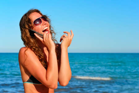 young smiling woman talking by phone on a beachの写真素材