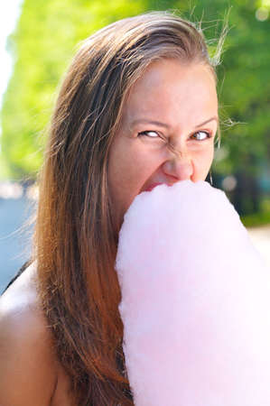 young beautiful woman is eating candyfloss in parkの写真素材