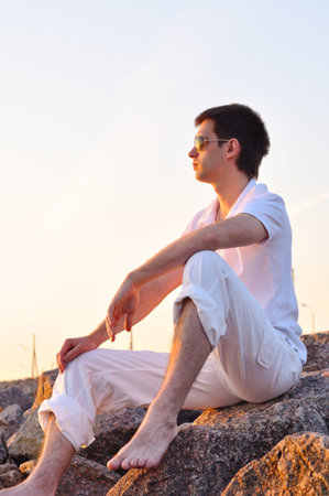 man is sitting on stones at sunriseの写真素材