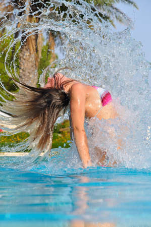 slim woman is spectacularly jumping out of pool and shaking hairの写真素材
