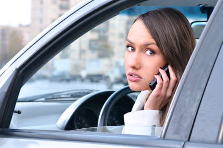 sensual young woman is looking at camera from a car and talking phoneの写真素材