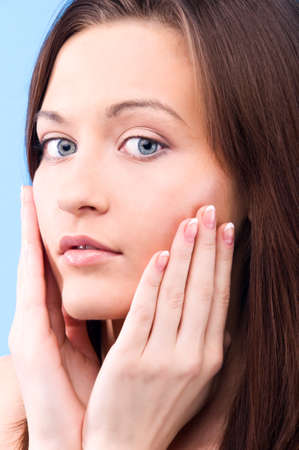 beautiful young woman is touching her face and looking at camera on blue backgroundの写真素材