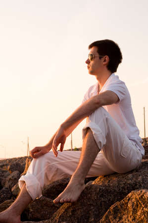 handsome man is sitting at stones at sunriseの写真素材