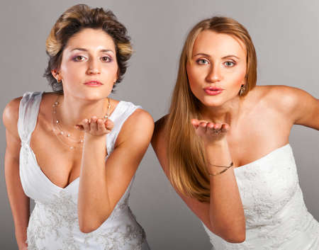 two beautiful brides is standing in wedding dress on grey background and blowing a kissesの写真素材